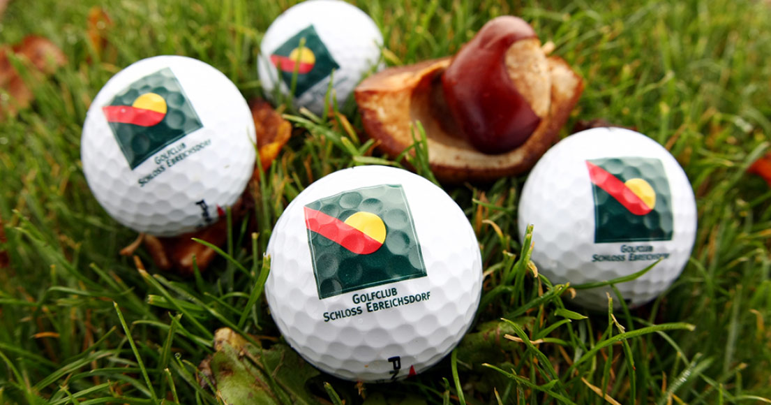 Vier weiße Golfbälle mit dem Aufdruck Golfclub Schloss Ebreichsdorf liegen in der Wiese